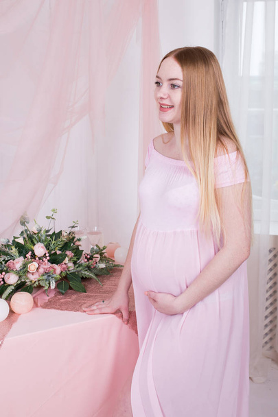 Woman during pregnancy in pink dress with flowers on backgroun - Φωτογραφία, εικόνα