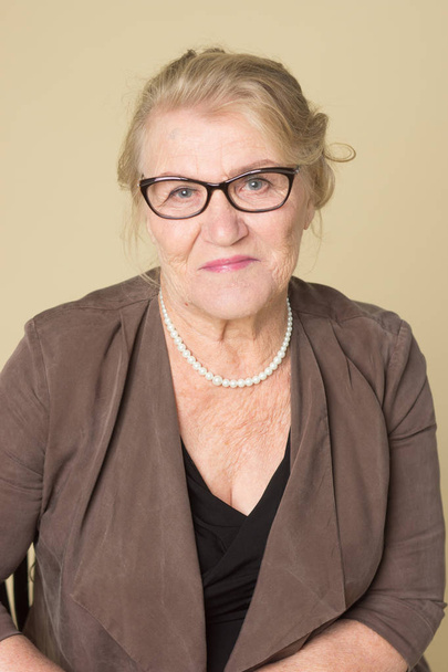 Portrait of an old woman wearing glasses on a beige background                  - Foto, imagen