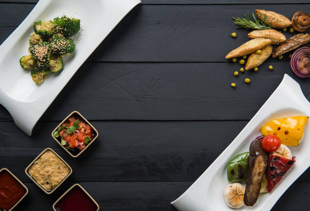 салаты, овощные продукты и соус в тарелках на черном деревянном фоне
 - Фото, изображение