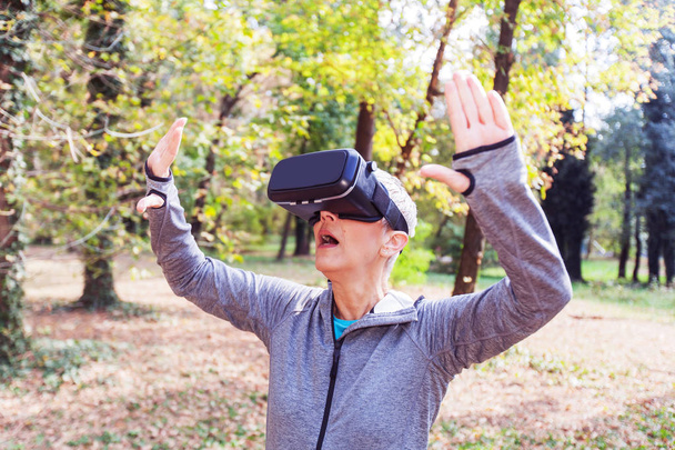 Сюрприз Старшая женщина весело с гарнитурой виртуальной реальности в лесу, устройство виртуальной реальности с использованием пожилых людей
. - Фото, изображение