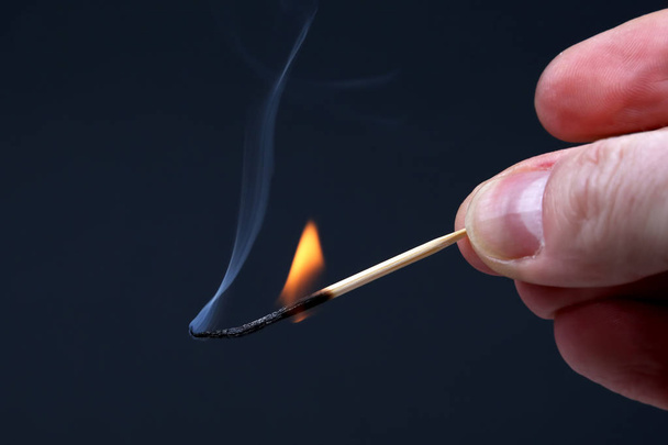 Burning and Smoking wooden match in hand on dark background - Photo, image