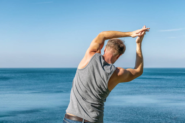 Hombre haciendo un ejercicio de calentamiento en el océano
. - Foto, Imagen
