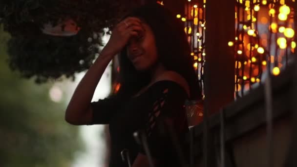 Gelukkig jongedame staat naast etalage, glimlacht en stuurt lucht kus op achtergrond van stadslichten om 's avonds. Bokeh-effect. - Video