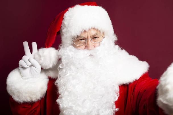 portrait of man in Santa Clause costume showing peace sign on red background, Christmas and New year concept  - Foto, Bild
