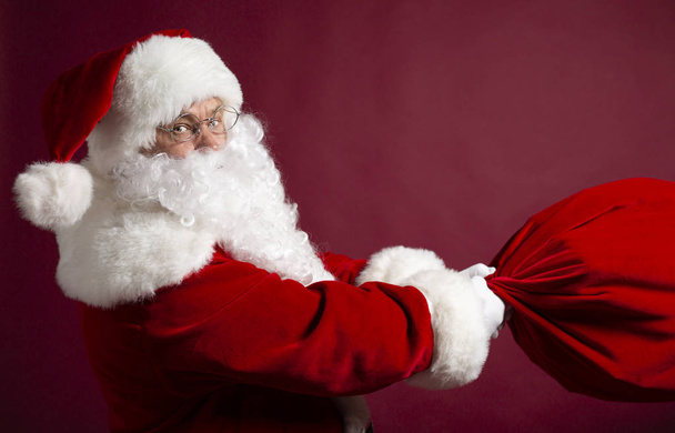 retrato de homem em Santa Cláusula traje segurando saco de presente em fundo vermelho, Natal e conceito de ano novo
   - Foto, Imagem