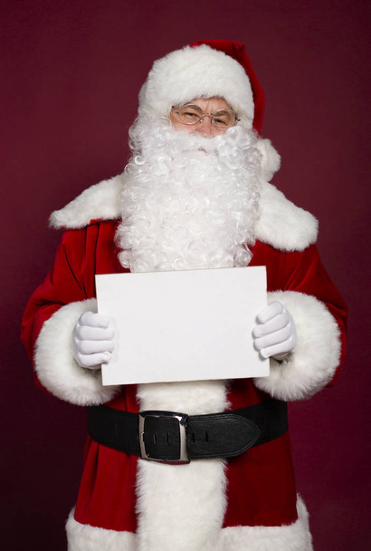 サンタ クロースの衣装が赤の背景に白い空白のバナーを押し、男性の肖像画クリスマスと新年のコンセプト  - 写真・画像