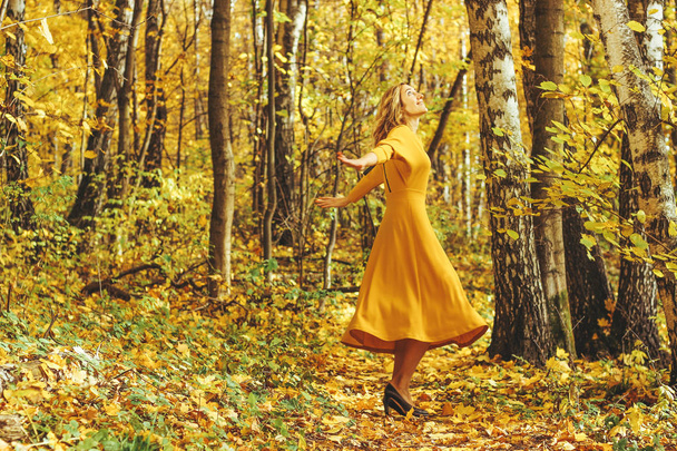 Young beautiful girl in a yellow long dress walks in autumn park with fallen leaves. - Φωτογραφία, εικόνα