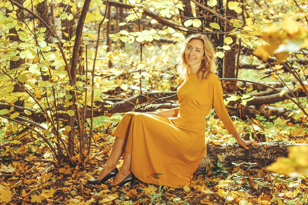 Young beautiful girl in a yellow long dress walks in autumn park with fallen leaves - Foto, imagen