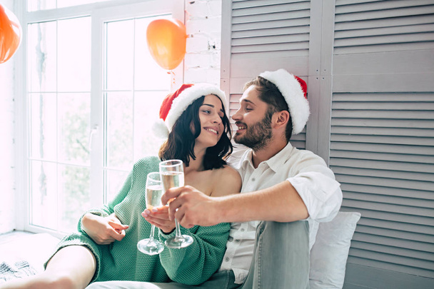 Happy couple in santa hats celebrating christmas with champagne in light bedroom  - Zdjęcie, obraz
