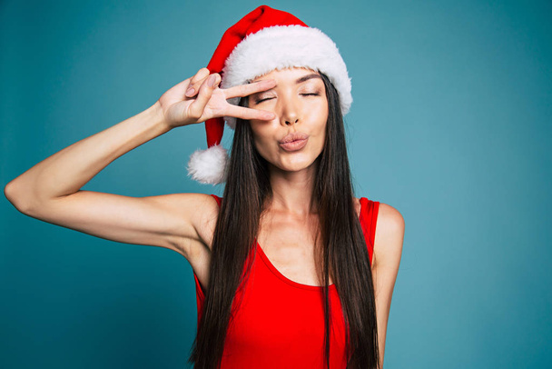 Brunette woman in santa hat and red swimsuit posing on blue background - Foto, imagen