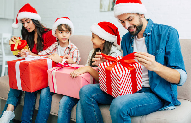 Young family in santa hats giving christmas presents in living room - Φωτογραφία, εικόνα