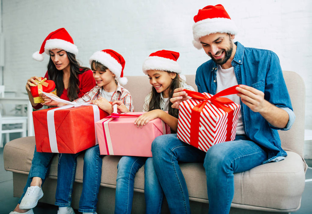 Young family in santa hats giving christmas presents in living room - Foto, Imagem