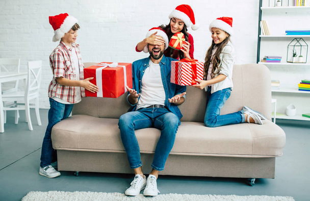 Cheerful family in santa hats giving christmas presents in living room - Фото, зображення
