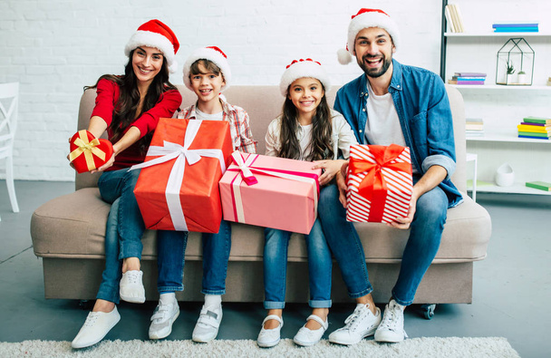 Cheerful family in santa hats giving christmas presents in living room - Photo, image
