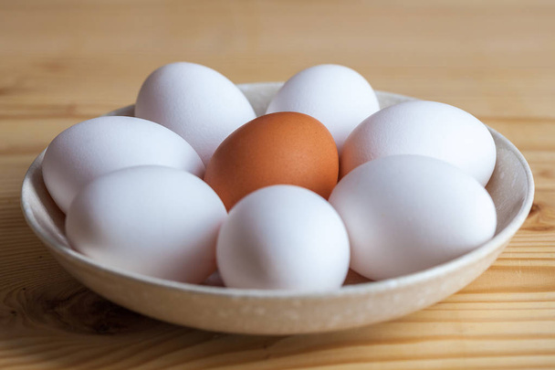One brown and white eggs in a ceramic dish on a wooden table. - Foto, Imagem