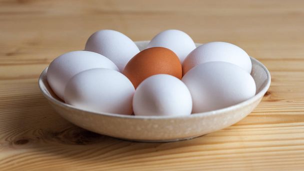 Jedno hnědé a bílé vejce v keramické misce na dřevěný stůl. - Fotografie, Obrázek