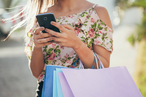 Shopper woman hand shopping with a smart phone and carrying bags - Foto, imagen