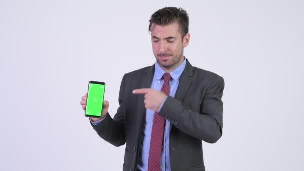 Young happy Hispanic businessman showing phone and giving thumbs up - Záběry, video