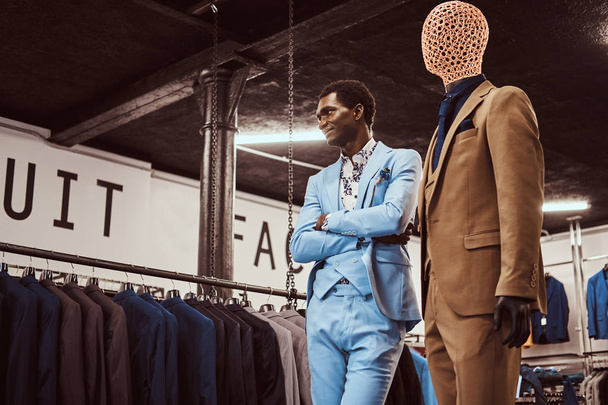 Elegánsan öltözött afro-amerikai ember közelében egy klasszikus férfi üzletben manöken keresztezett karokkal pózol. - Fotó, kép