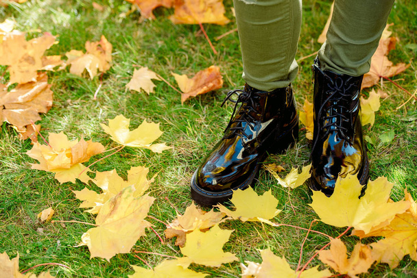 女性で足の上に立って黒のパテント レザー ブーツ黄色落ちたもみじの絨毯葉秋の公園で歩いている間。温かみのある居心地の良い秋のコンセプト - 写真・画像