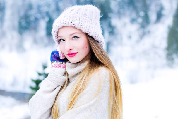 Detail tváře dívčí svetr a čepice, která vypadá v objektivu fotoaparátu na pozadí sněhu a dřevo - Fotografie, Obrázek