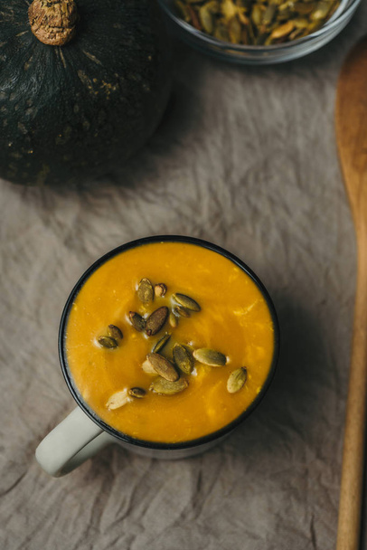 Плоская укладка сливочного тыквенного супа с семенами в чашке, за скатертью, зимняя теплая еда
 - Фото, изображение