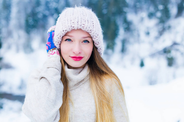 女の子の帽子に彼女の手を保持しているし、雪と森林の背景にカメラのレンズを見て - 写真・画像