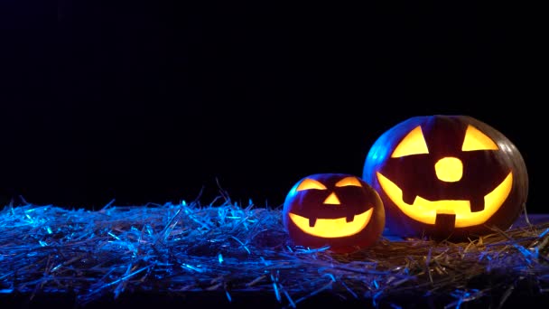 Two Halloween pumpkins are burning bright flames inside are standing on hay. Black background - Footage, Video