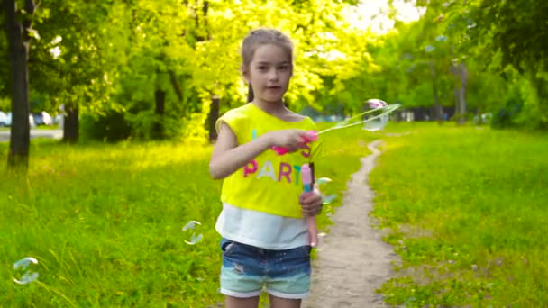 Malá dívka si hraje s mýdlovými bublinami v letním parku - Záběry, video