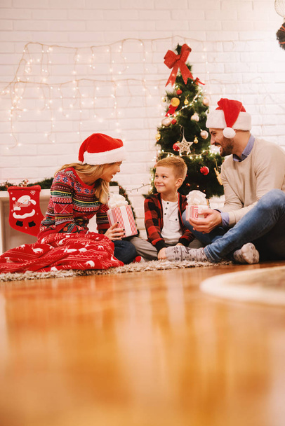 ευτυχισμένη οικογένεια γιορτάζει τα Χριστούγεννα στο σπίτι κάθεται στο πάτωμα κάτω από καρό κοντά στο χριστουγεννιάτικο δέντρο  - Φωτογραφία, εικόνα