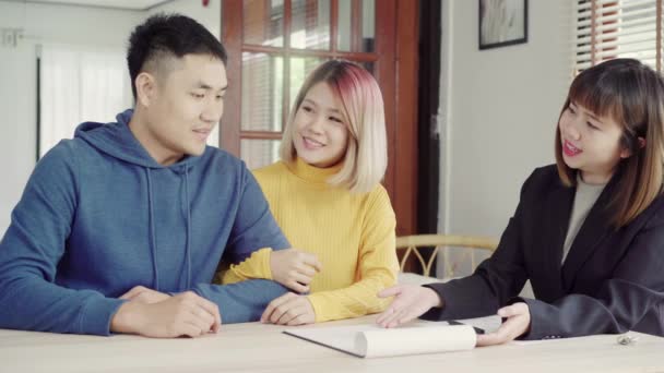 Happy young Asian couple and realtor agent. Cheerful young man signing some documents while sitting at desk together with his wife. Buying new house real estate. Signing good condition contract. - Footage, Video
