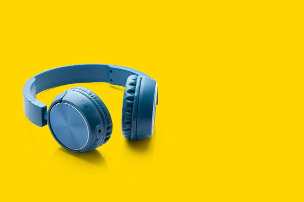 blauwe Bluetooth hoofdtelefoon op gele achtergrond packshot Studioapparatuur - Foto, afbeelding