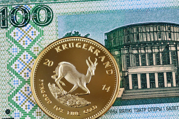 A close up image of a golden krugerrand against the background of a 100 Belorussian ruble note - Photo, Image