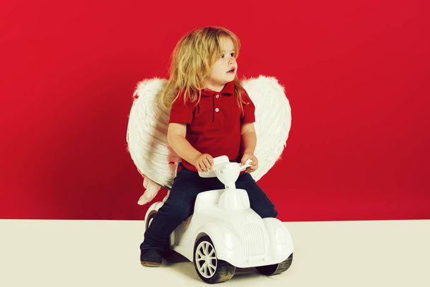angel little boy on red background on car toy - Photo, image