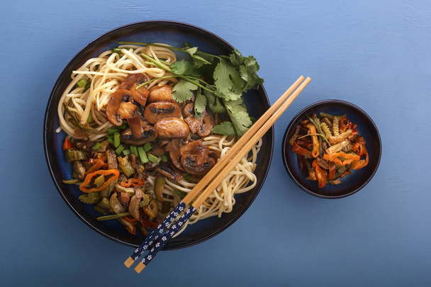 Chinese noodles with mushrooms, vegetables and herbs on the blue table. Top view - Photo, Image