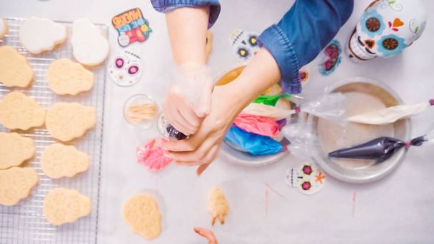 Overhead view of hands of woman decorating sugar skull cookies with royal icing for Dia de los Muertos holiday. - Valokuva, kuva