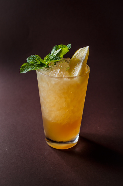 Bicchiere di cocktail all'arancia con menta, ghiaccio e fetta di arancia su elegante sfondo marrone scuro
. - Foto, immagini
