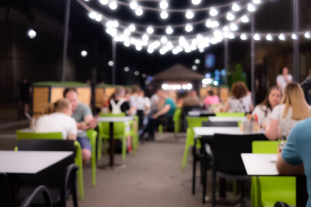 Homályos kép a night Fesztivál egy étteremben. Boldog és pihentető emberek a kávézó asztal - Fotó, kép
