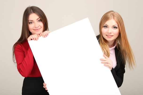 Two business women with blank form on grey background - Photo, image