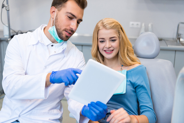 happy young dentist showing tablet to female client in dental chair - Fotoğraf, Görsel