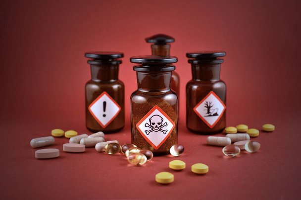 Vial of poison stock images. Vial with warning pictogram stock images. Laboratory accessories on a red background. Brown glass containers. Brown chemical glass - Photo, Image