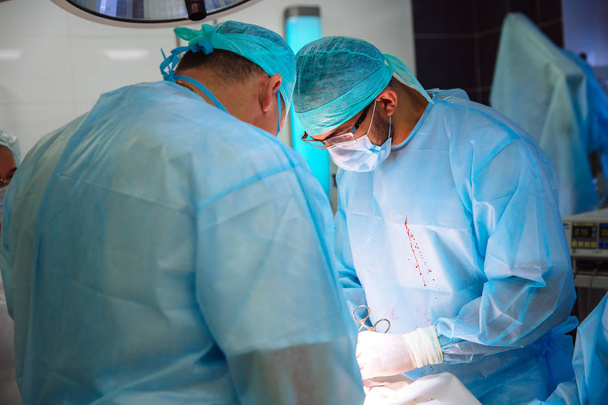 Двоє лікарів у стерильному медичному одязі проводять операцію в лікарні. Професійна робота в клініці, хірурги чоловіки з помічницею жінки. Поняття здоров'я, медицина
. - Фото, зображення