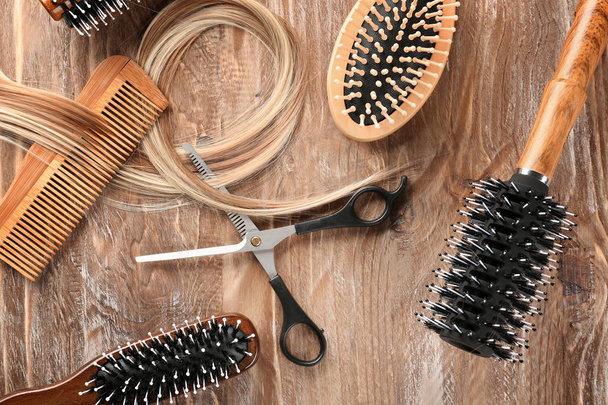 Flat lay composition with hairdresser's tools and strand of blonde hair on wooden background - Fotoğraf, Görsel