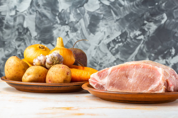 Kawałek wieprzowa i cebuli, czosnku, ziemniaki, marchew i buraki w zbliżeniu talerze glina. Zestaw świeże składniki do gotowania zupy. Koncepcja domowe jedzenie. Miejsce - Zdjęcie, obraz