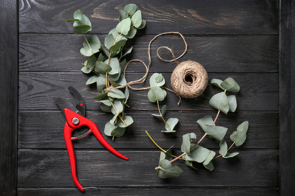 Zelená eukalyptu větve s nůžky a klubíčko provázku na tmavý dřevěný stůl - Fotografie, Obrázek