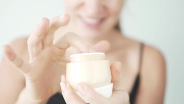 Happy girl holding in her hands a jar with a new face cream - Materiał filmowy, wideo