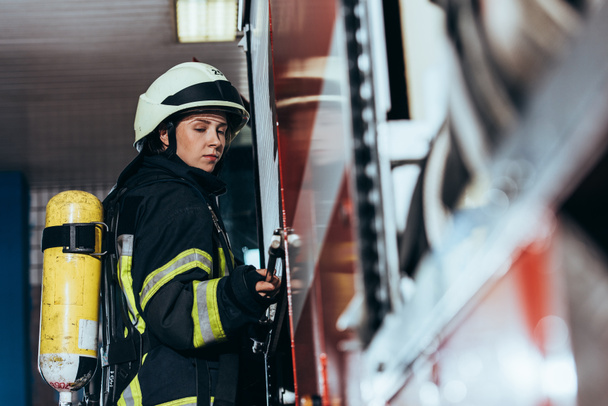 oldalnézetből női tűzoltó a tűzoltó készülék vissza a tűzoltóállomás teherautó bezárása - Fotó, kép
