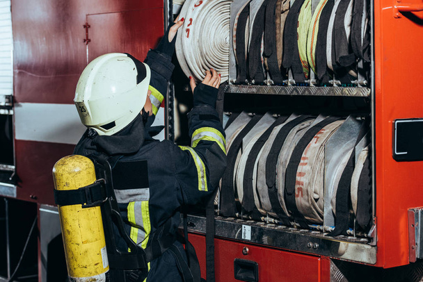 частковий вигляд жіночого пожежника, який вставляє водяний шланг у вантажівку під час пожежної служби
 - Фото, зображення