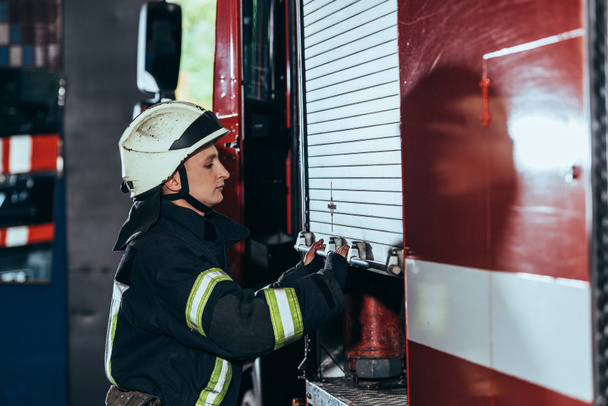 side view of fireman in uniform closing truck at fire department - Foto, Imagen