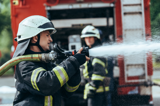 selective focus of firefighter with water hose extinguishing fire on street - Photo, Image